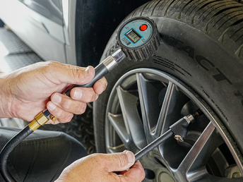 Technician checking car tire pressure with a digital tire pressure gauge during vehicle maintenance in an auto service garage.